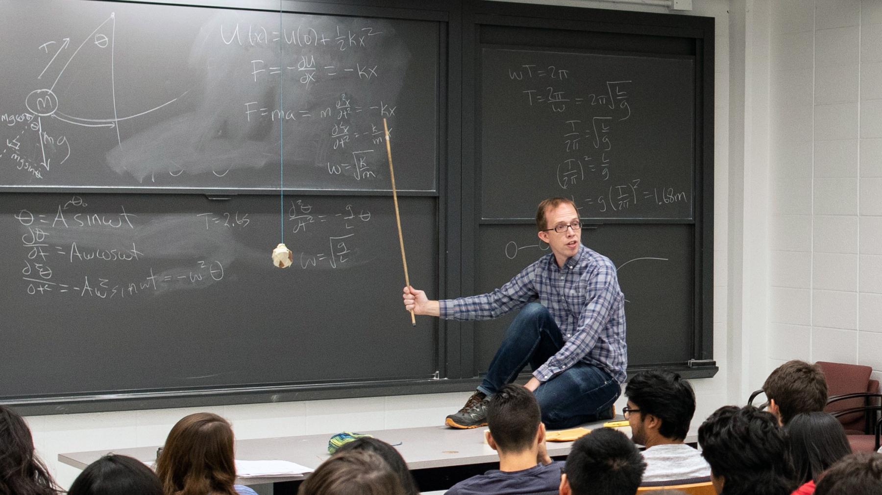 Andrew Houck, perched on the table in front of his class.