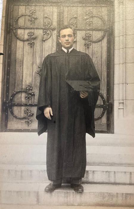 Joe Schein, dressed in his graduation gown, on the marble steps of a Princeton building