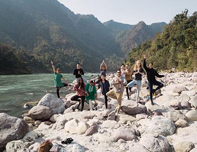 A group of people standing in yoga poses on rocks beside a river