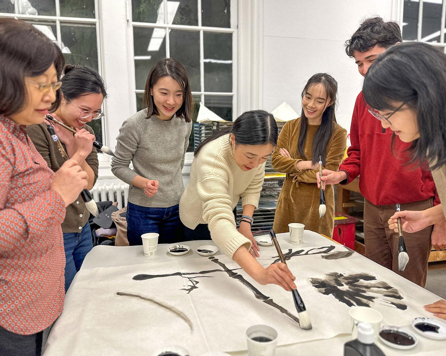 Beijing-based artist Peng Wei painting on a table, surrounded by students.